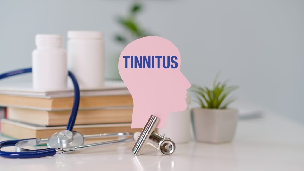 The word tinnitus on a paper head cutout on a desk with medical instruments